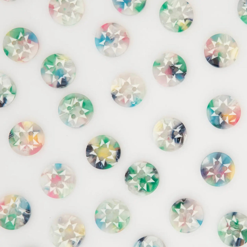 A close-up arrangement of small round iridescent buttons with star-shaped print, scattered on a plain white background.