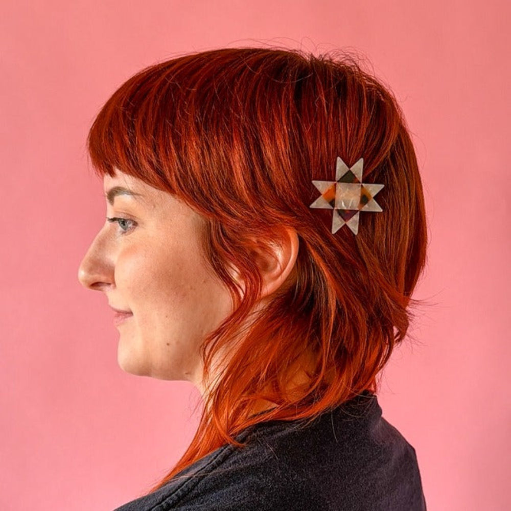 Person with red hair wearing a decorative hair clip against a pink background