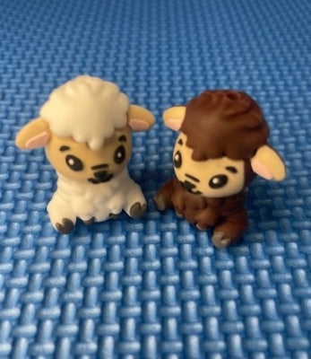 Two small sheep point protectors, one white and one brown, on a blue textured surface.
