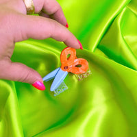 Small scissor hair claw held by a hand on a bright green background