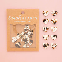 Sarah Hearts premium buttons in a tortoise shell print pattern, shown in their kraft paper packaging on the left and ten individual buttons displayed on the right against a solid pink background.