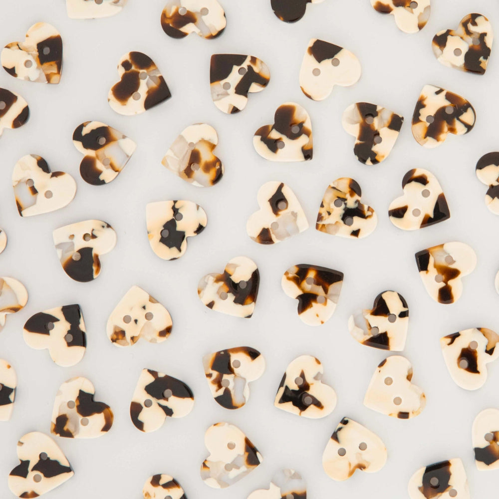 Heart-shaped buttons with a tortoiseshell pattern in cream, brown, and black, scattered on a light gray background.