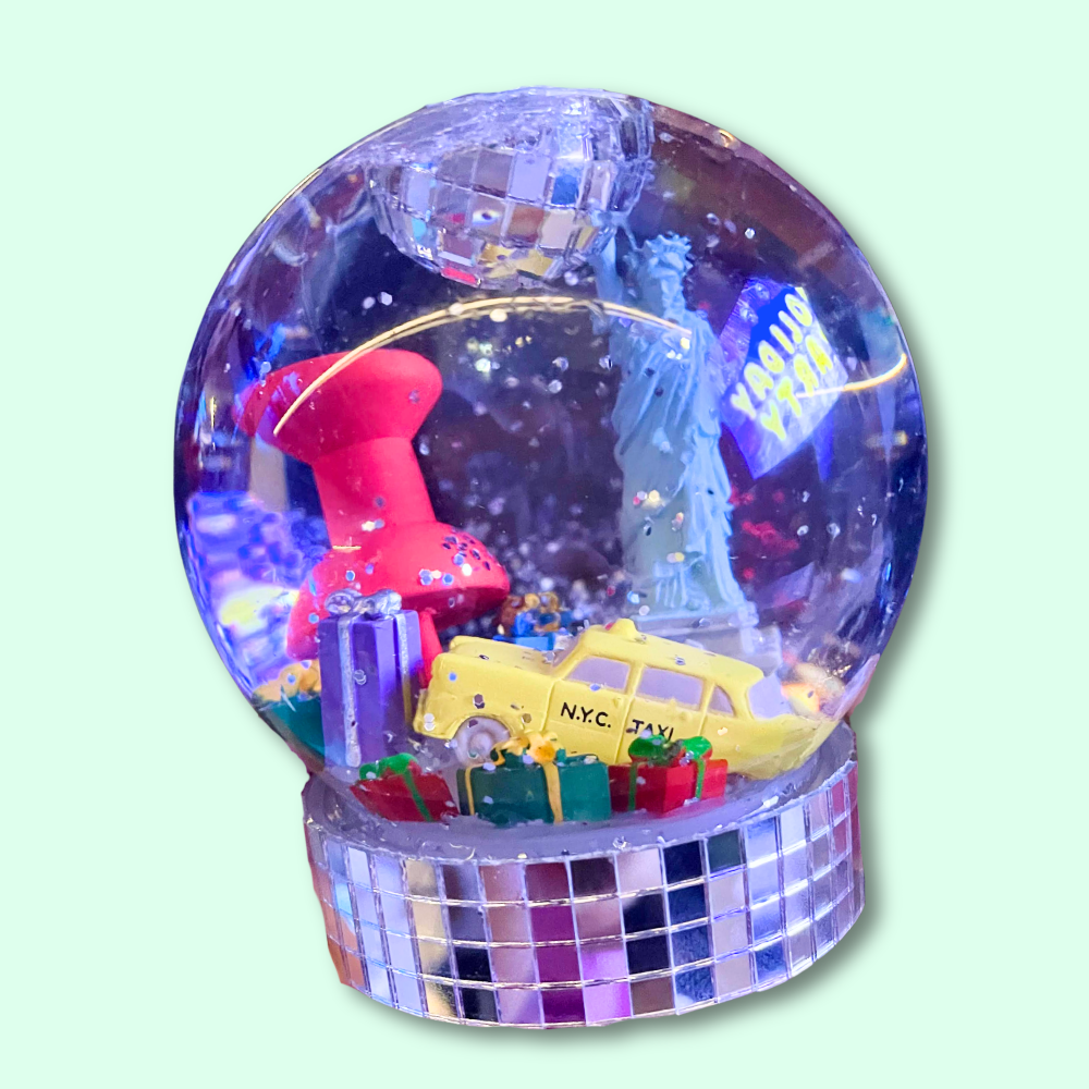 Colorful snow globe with a pink building, yellow taxi, and Statue of Liberty on a light green background