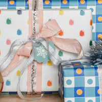 Gift wrapped in polka dot paper with ribbons and a tag on a checkered background