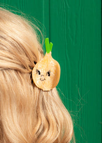 Hair clip shaped like a cartoon onion with a face on a person's hair against a green background
