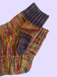 The cuffs and heels of a pair of colorful knit socks on a lavender background.