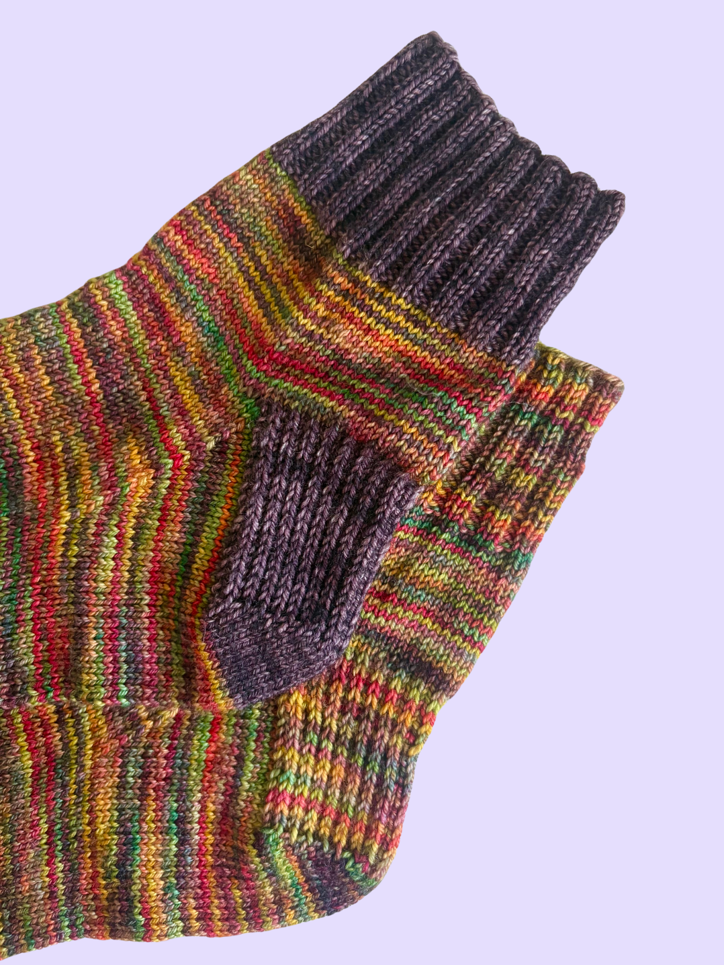 The cuffs and heels of a pair of colorful knit socks on a lavender background.