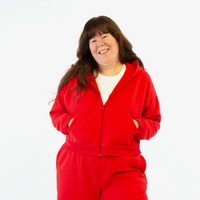 A woman in a cropped bright red zipper hoodie stands with her hands in her pockets