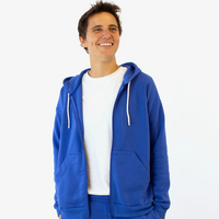 A man in a bright blue zipper hoodie with pockets stands against a white wall