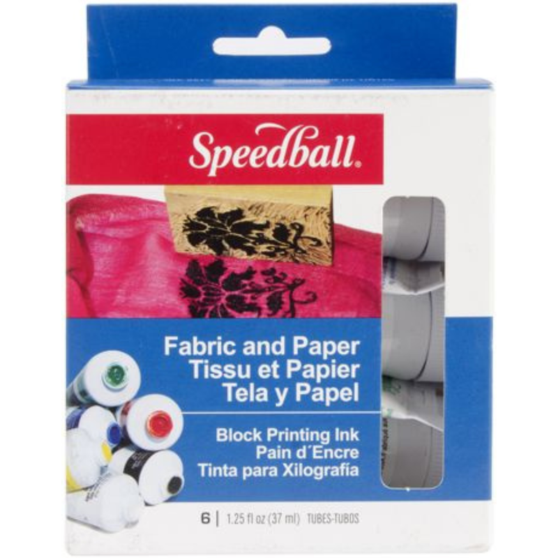 Speedball fabric and paper block printing ink set in its retail packaging, featuring a white box with blue and red branding, a photo of a wooden stamp on pink fabric, and a clear window showing six gray ink tubes inside.
