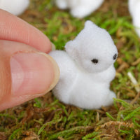 Small white fuzzy squirrel held between fingers on a green mossy background.