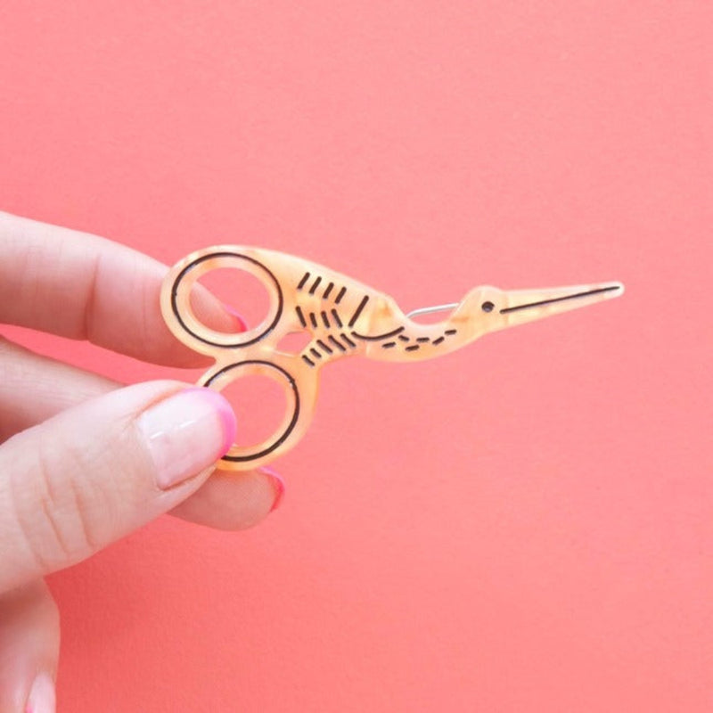 Small stork scissors  pin held by a hand against a pink background