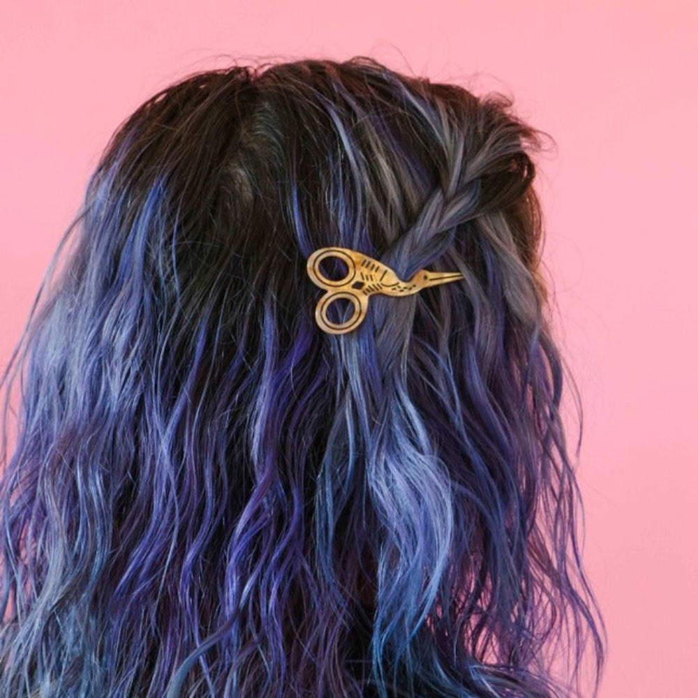 Hair with blue and black color, featuring a decorative gold scissors hair clip against a pink background.