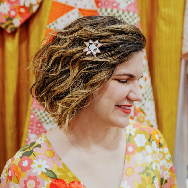 Woman with a decorative hair clip wearing a floral outfit in front of a colorful quilt.