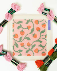 Needlepoint canvas with a strawberry design surrounded by colorful skeins of thread