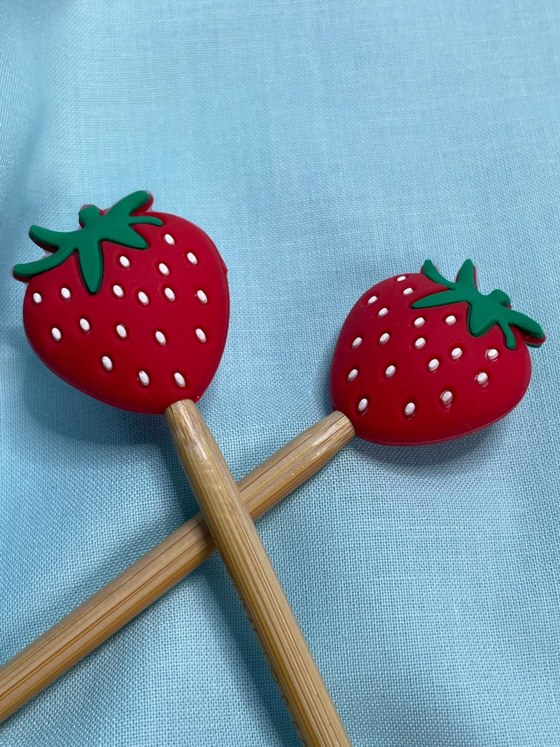 Two strawberry-shaped silicone ends on needles on a light blue background.