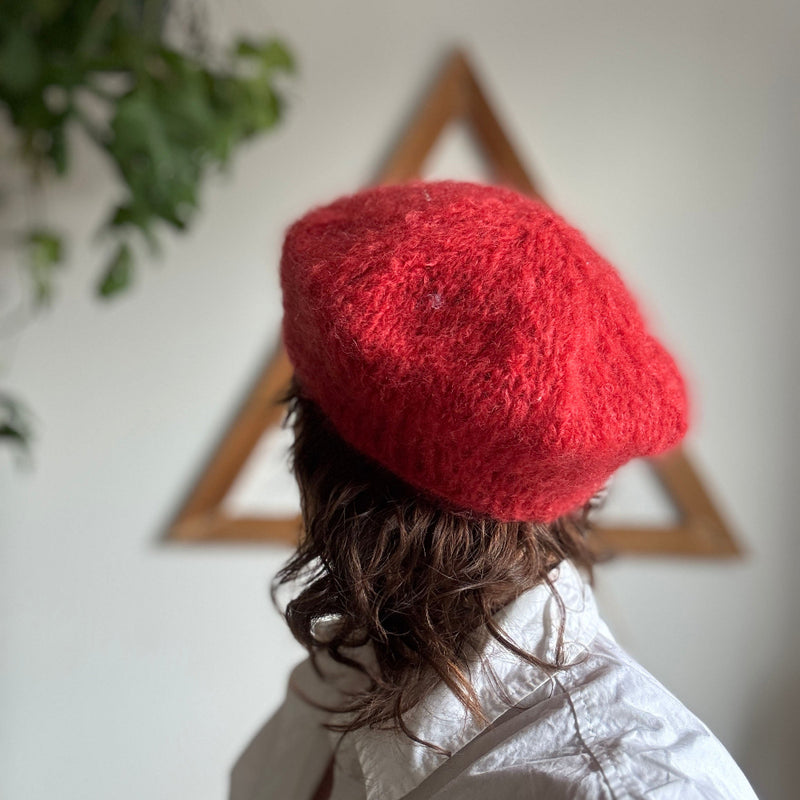 Person wearing a red knitted hat with a white wall and plant in the background