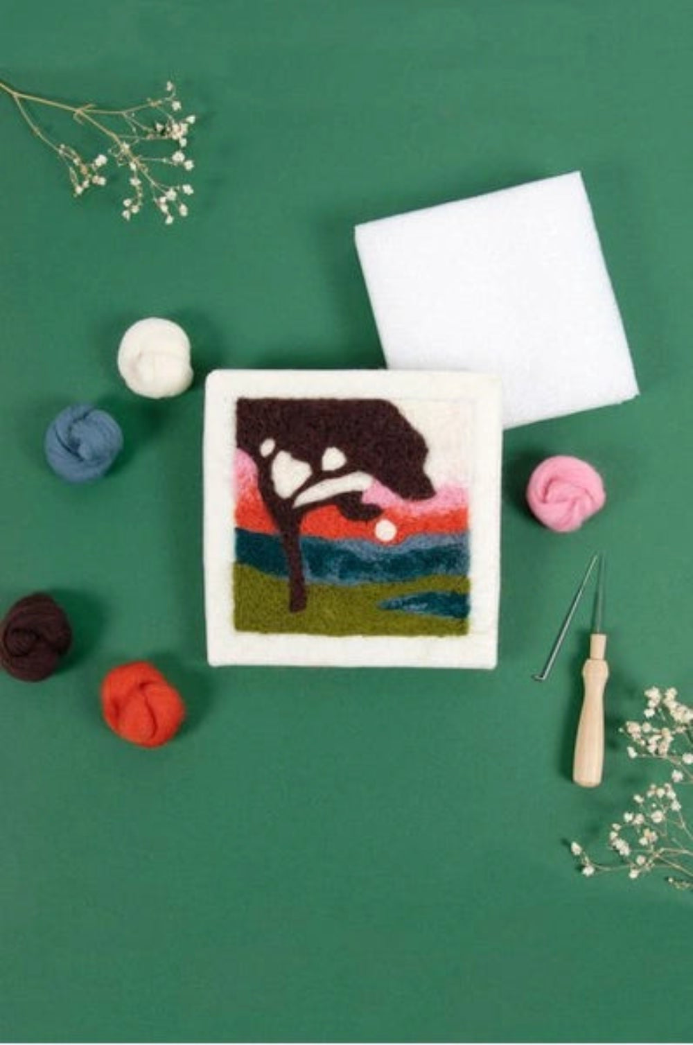 Felted canvas with a black tree design on a green background with fabric and embroidery tools.
