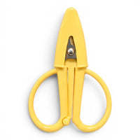 A small butter yellow pair of scissors with a matching point protector on a white background
