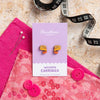 Wooden tape measure earrings with packaging on a pink fabric background