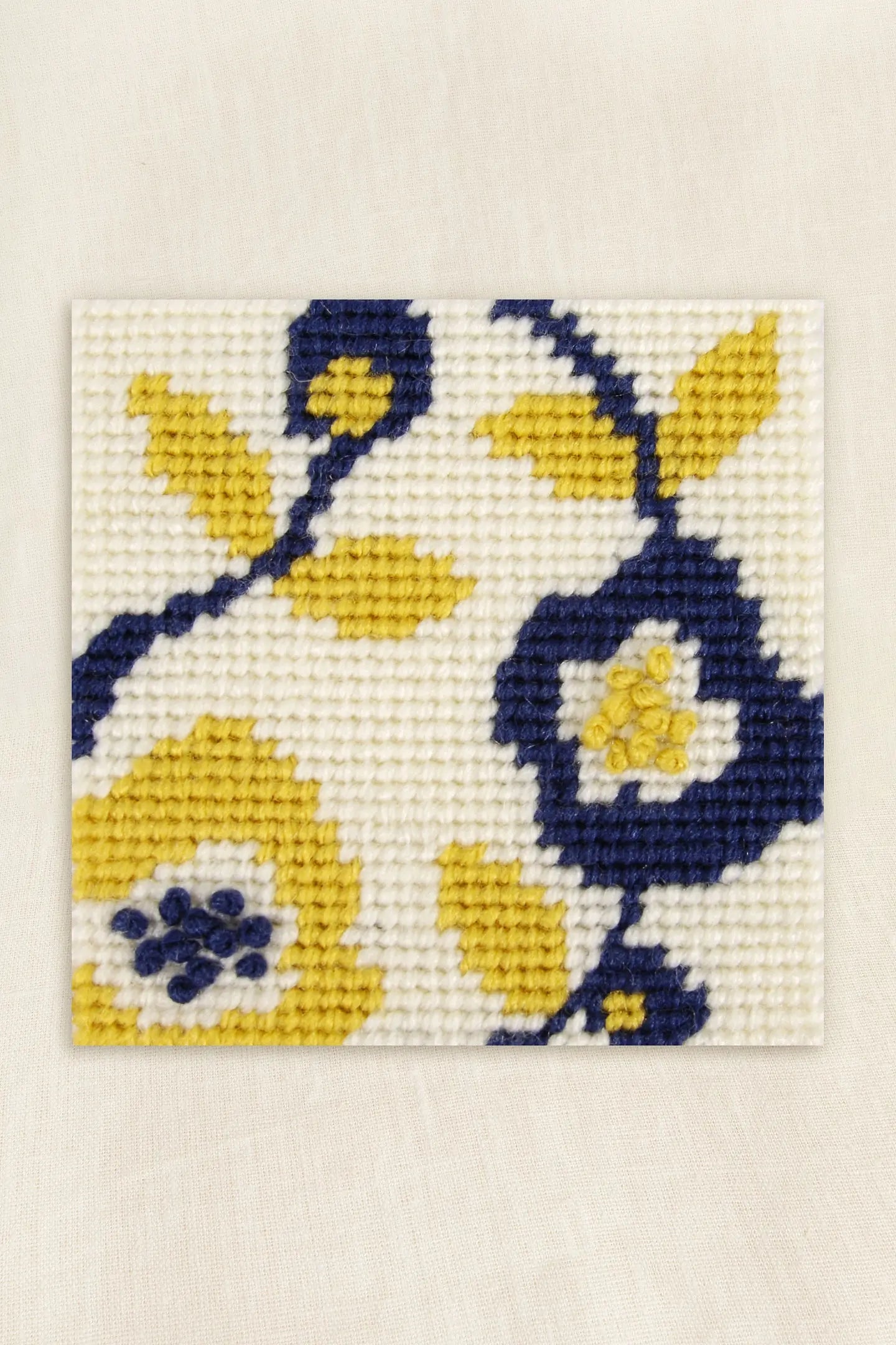 Needlepointed floral design with yellow and blue flowers on a white background
