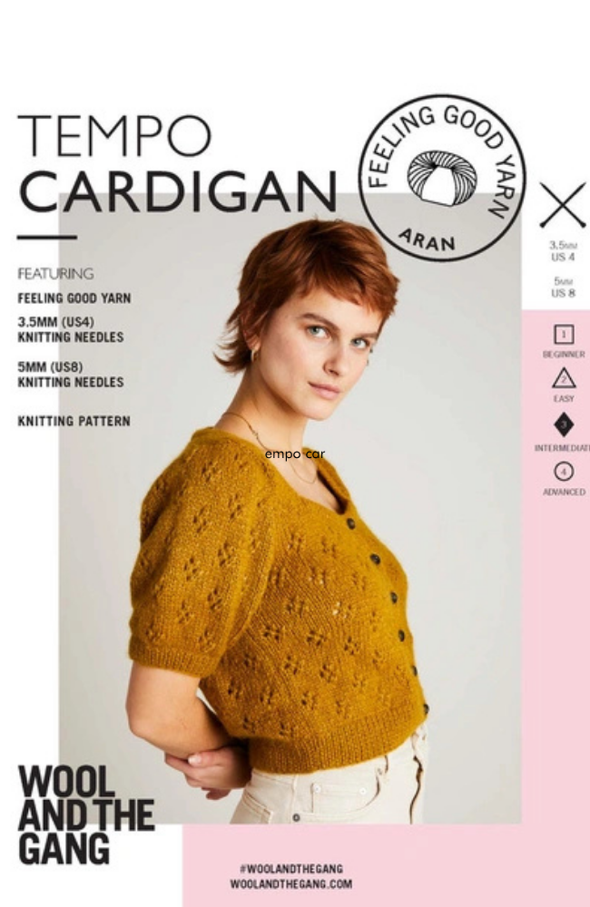 Shirt red haired woman wearing white jeans and a light brown short sleeved lace cardigan on a gray, pink, and white background with Wool and the Gang branding and text.