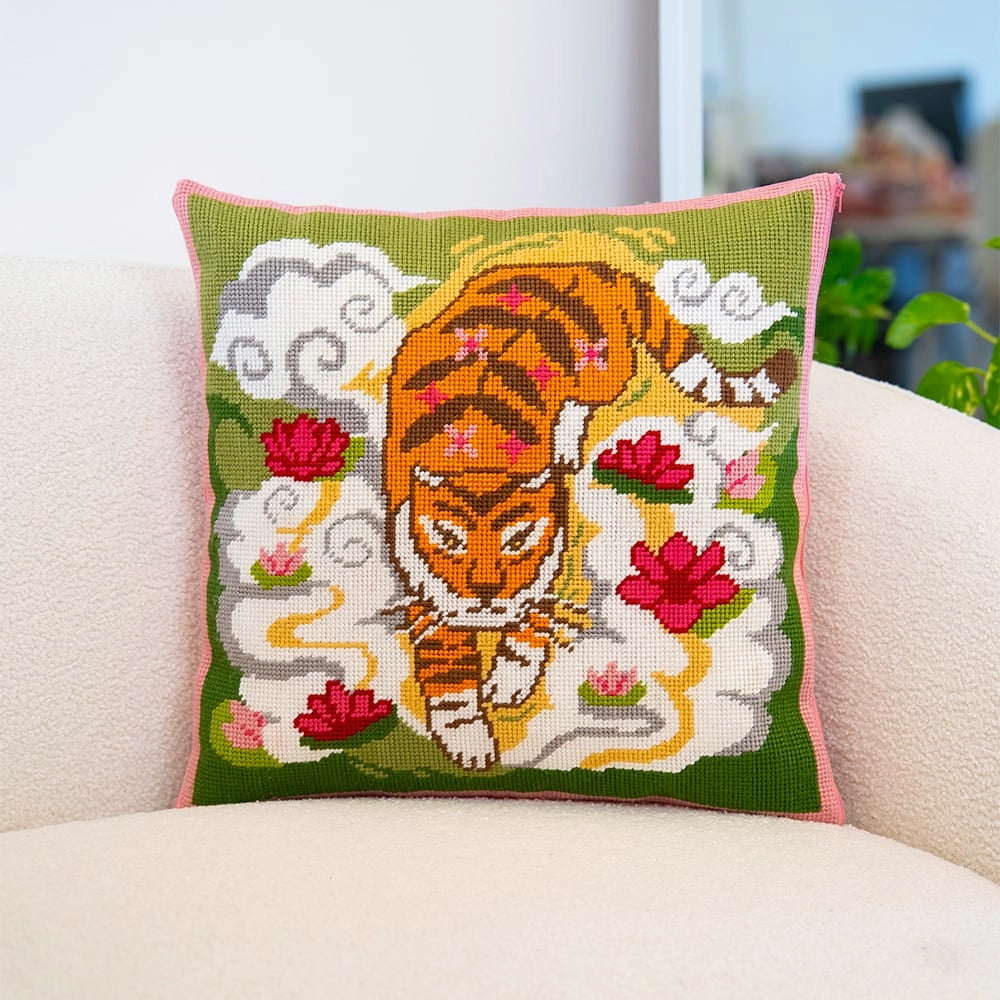 A needlepoint cushion with a central orange tiger amongst clouds and red lotus flowers on a green background.