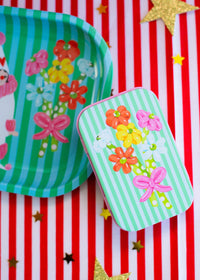 Colorful paper plates and tin with floral and bow designs on a red and white striped background.