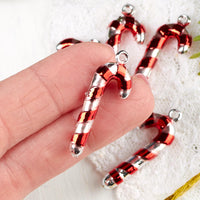 Red and silver candy cane-shaped charms held by a hand on a white fabric background