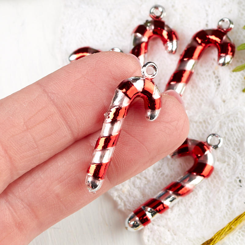 Red and silver candy cane-shaped charms held by a hand on a white fabric background