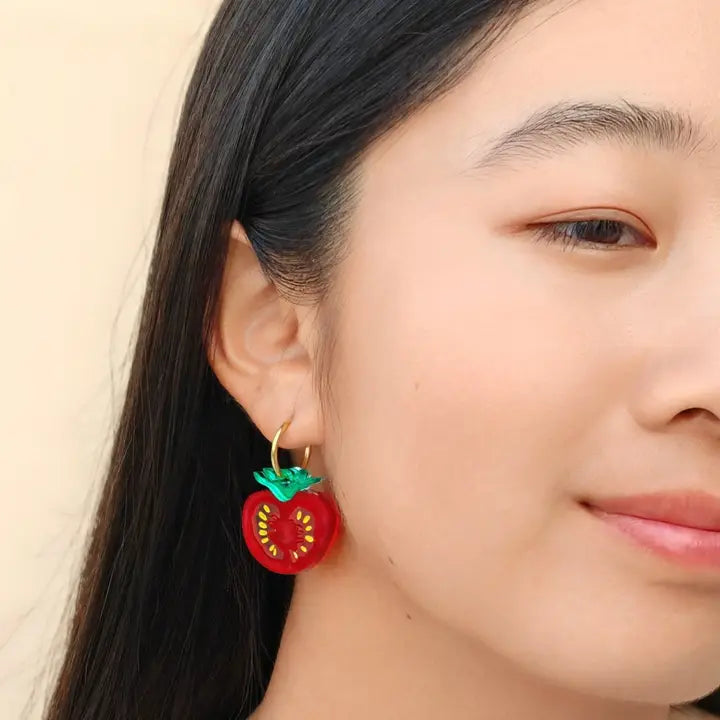 Close-up of a person wearing a red tomato-shaped earring with green leaves.