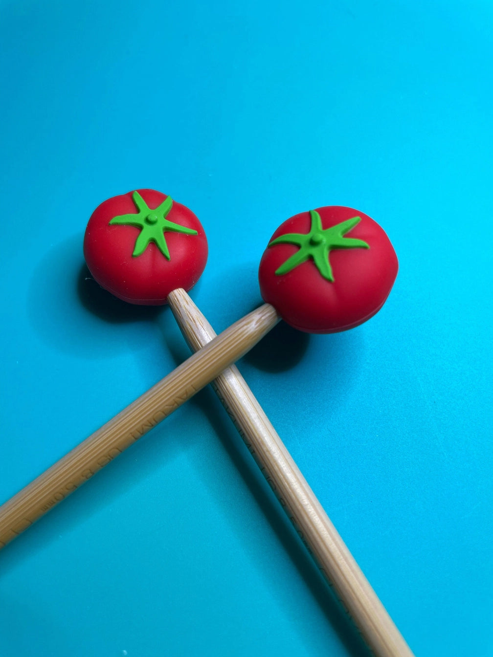 Two wooden needles with tomato-shaped ends on a blue background.
