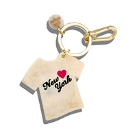 Charm shaped like a white t-shirt with black text reading "New York" and a red heart on a gold keychain ring.