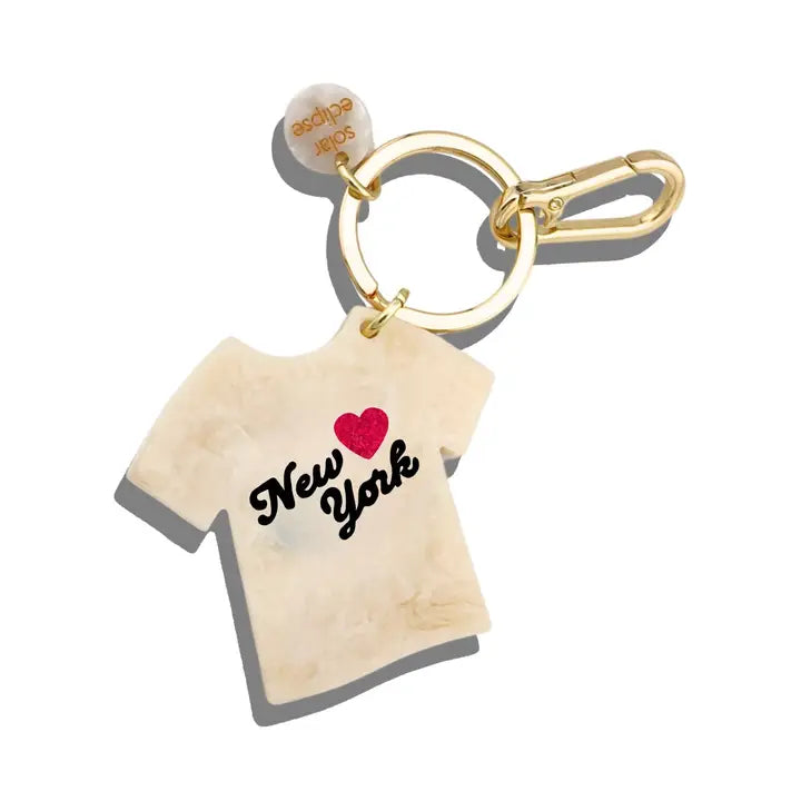 Charm shaped like a white t-shirt with black text reading "New York" and a red heart on a gold keychain ring.
