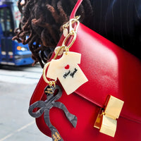 Red handbag with decorative keychain featuring bow and t-shirt charms on a city street.
