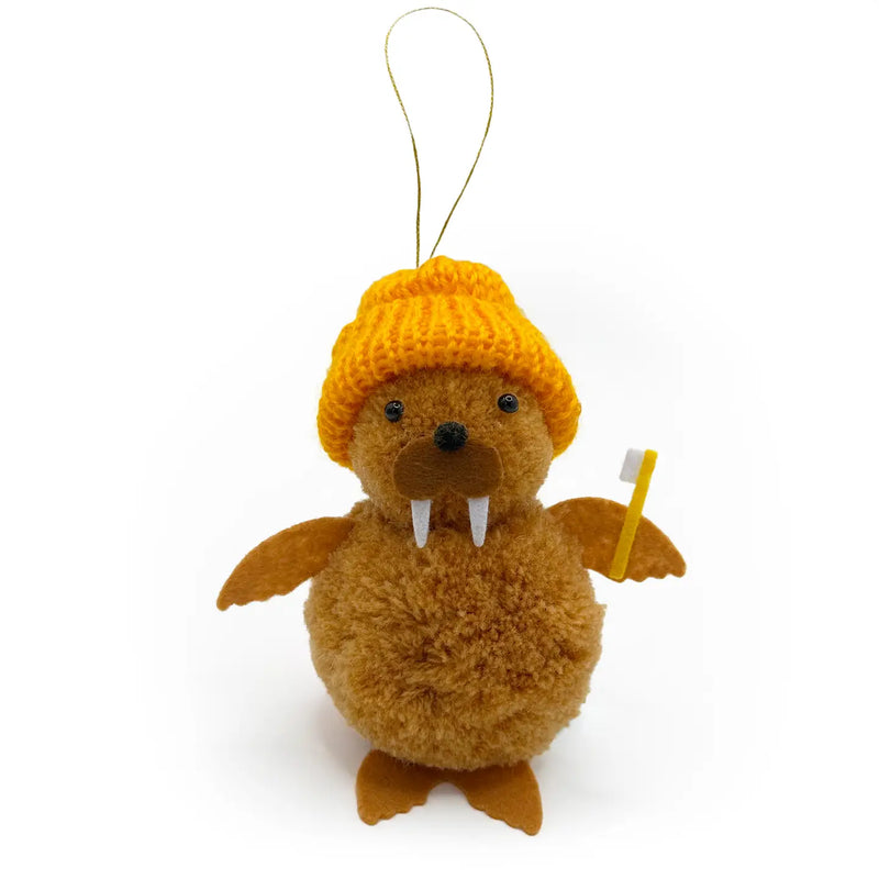 Brown walrus with orange knit hat holding a toothbrush pom pom ornament on a white background.