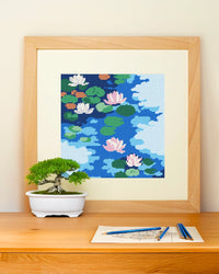 Framed needlepoint artwork with a floral design resting on a wooden table against a white background