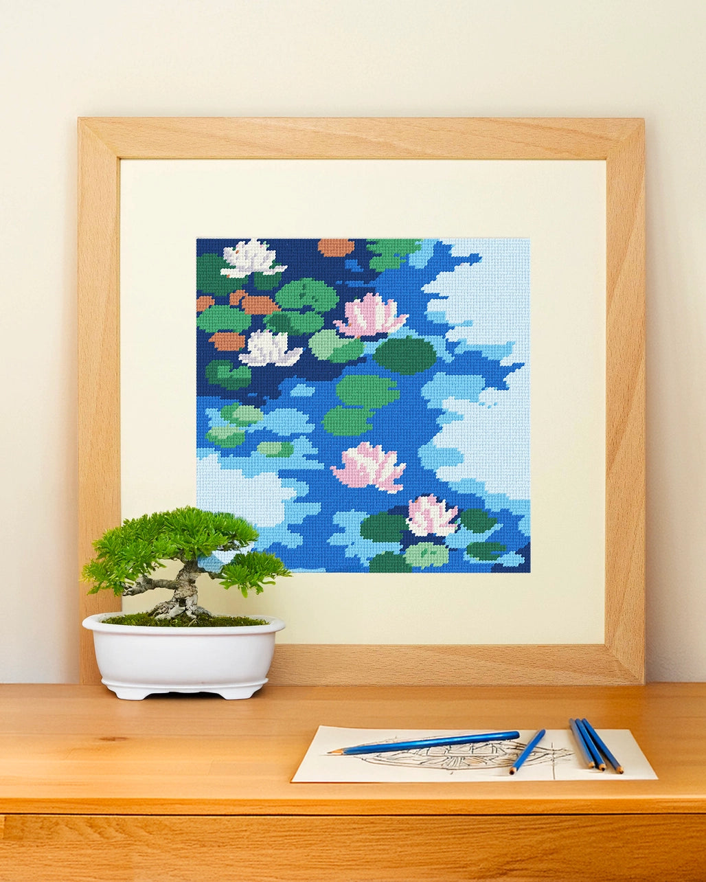 Framed needlepoint artwork with a floral design resting on a wooden table against a white background