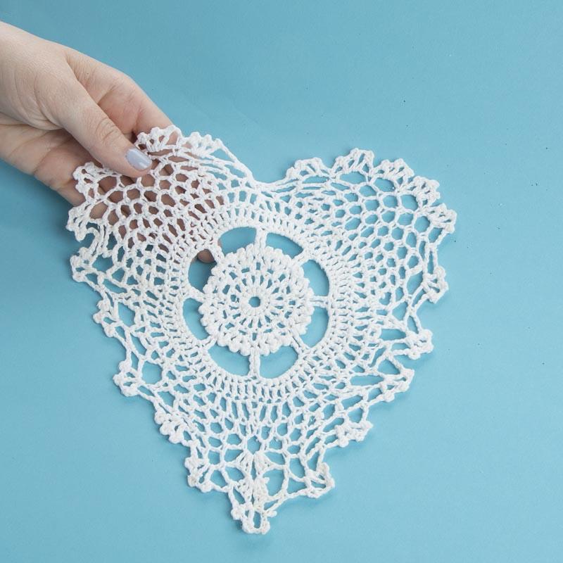 Hand holding a white crocheted heart-shaped doily against a blue background