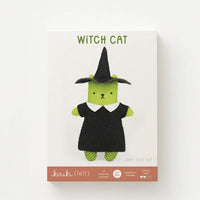 A box with the words "WITCH CAT" showing a felt toy shaped like a cat dressed in a witch costume, featuring a green body, a black dress with a white collar, and a black witch hat, set against a plain white background.