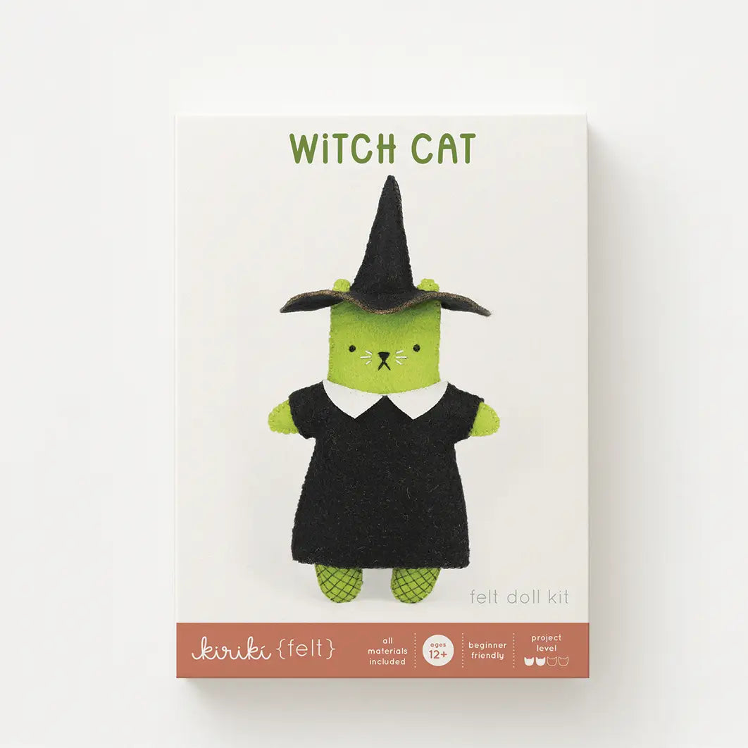 A box with the words "WITCH CAT" showing a felt toy shaped like a cat dressed in a witch costume, featuring a green body, a black dress with a white collar, and a black witch hat, set against a plain white background.