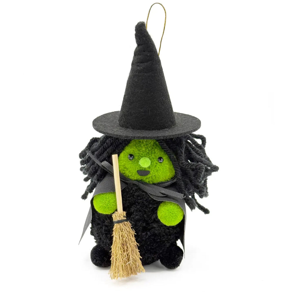 A small witch plush ornament with a black pointed hat, black dress, bright green face and hands, and a straw broom, photographed on a plain white background.