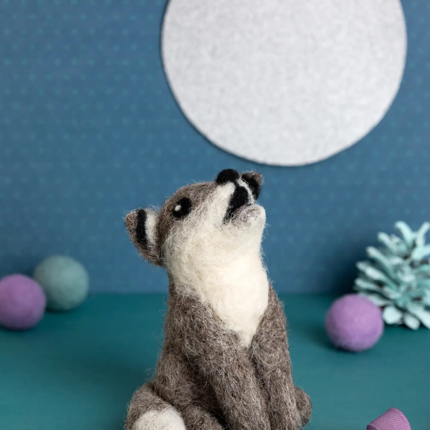 Needle felted wolf toy sitting on a teal surface with a blue background