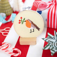 Cross-stitched robin design on a hoop with Christmas-themed background