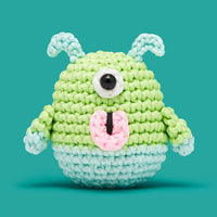 Crocheted green and blue creature with a single eye on a teal background